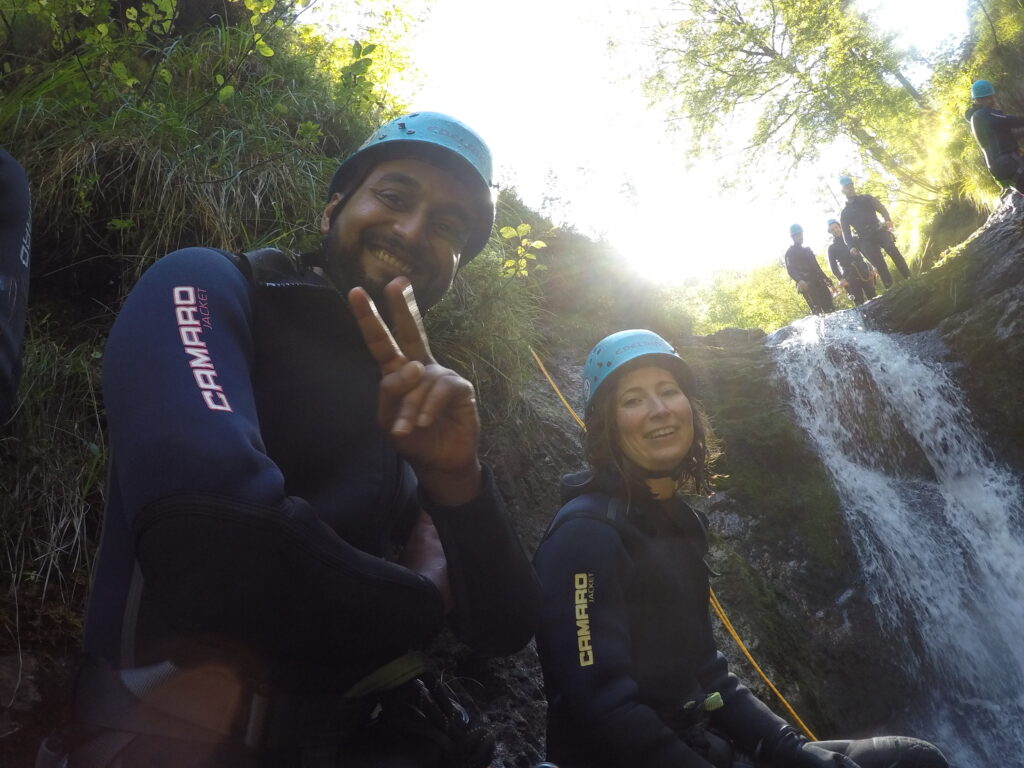 accilium employees in neoprene suits and equipped with climbing gear and helmets wandering through a guided canyoning tour in a mountain stream