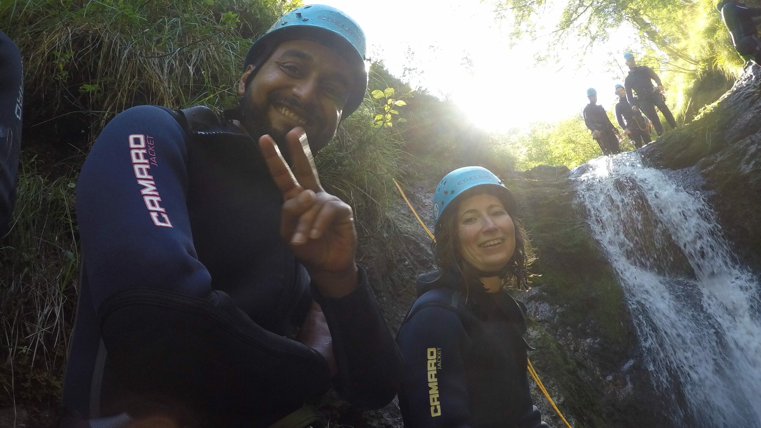 accilium employees in neoprene suits and equipped with climbing gear and helmets wandering through a guided canyoning tour in a mountain stream