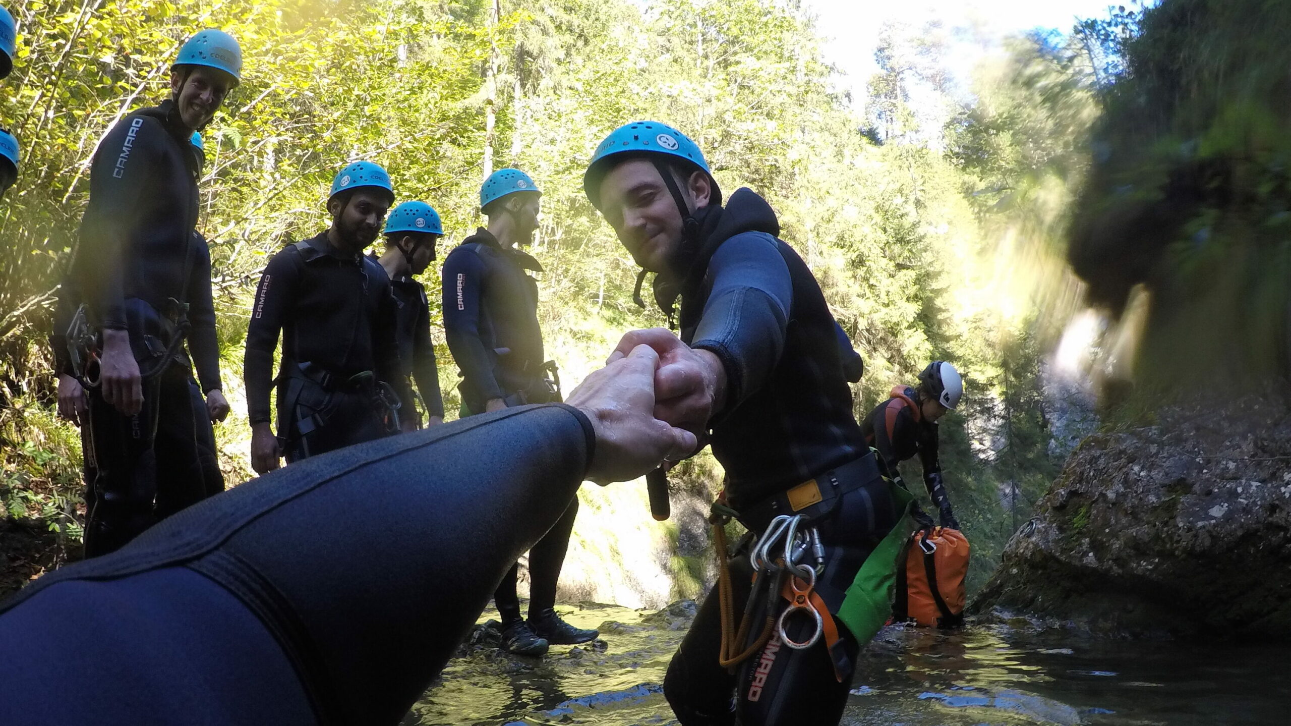 One accilium employee is helping the other who is holding the camera out of the water inside a canyon by giving him a hand.