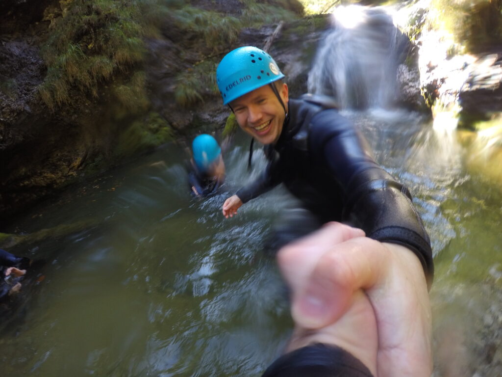 accilium employees in neoprene suits and equipped with climbing gear and helmets wandering through a guided canyoning tour in a mountain stream