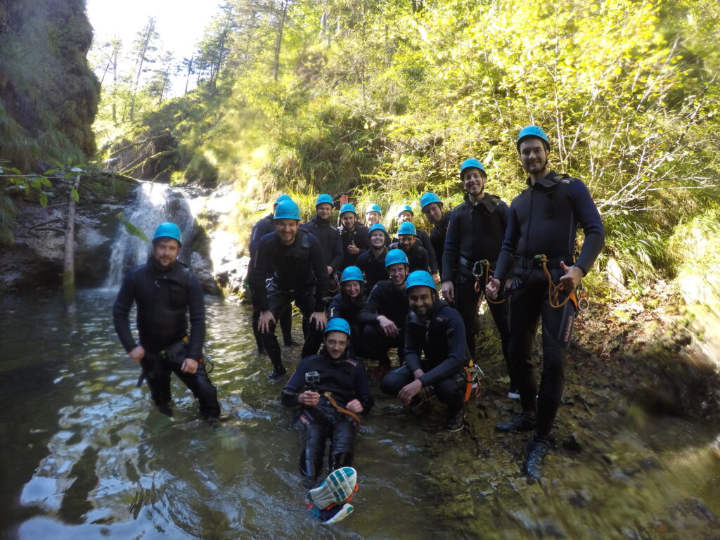 16 accilium employees in neoprene suits and equipped with climbing gear and helmets are standing inside a canyon.