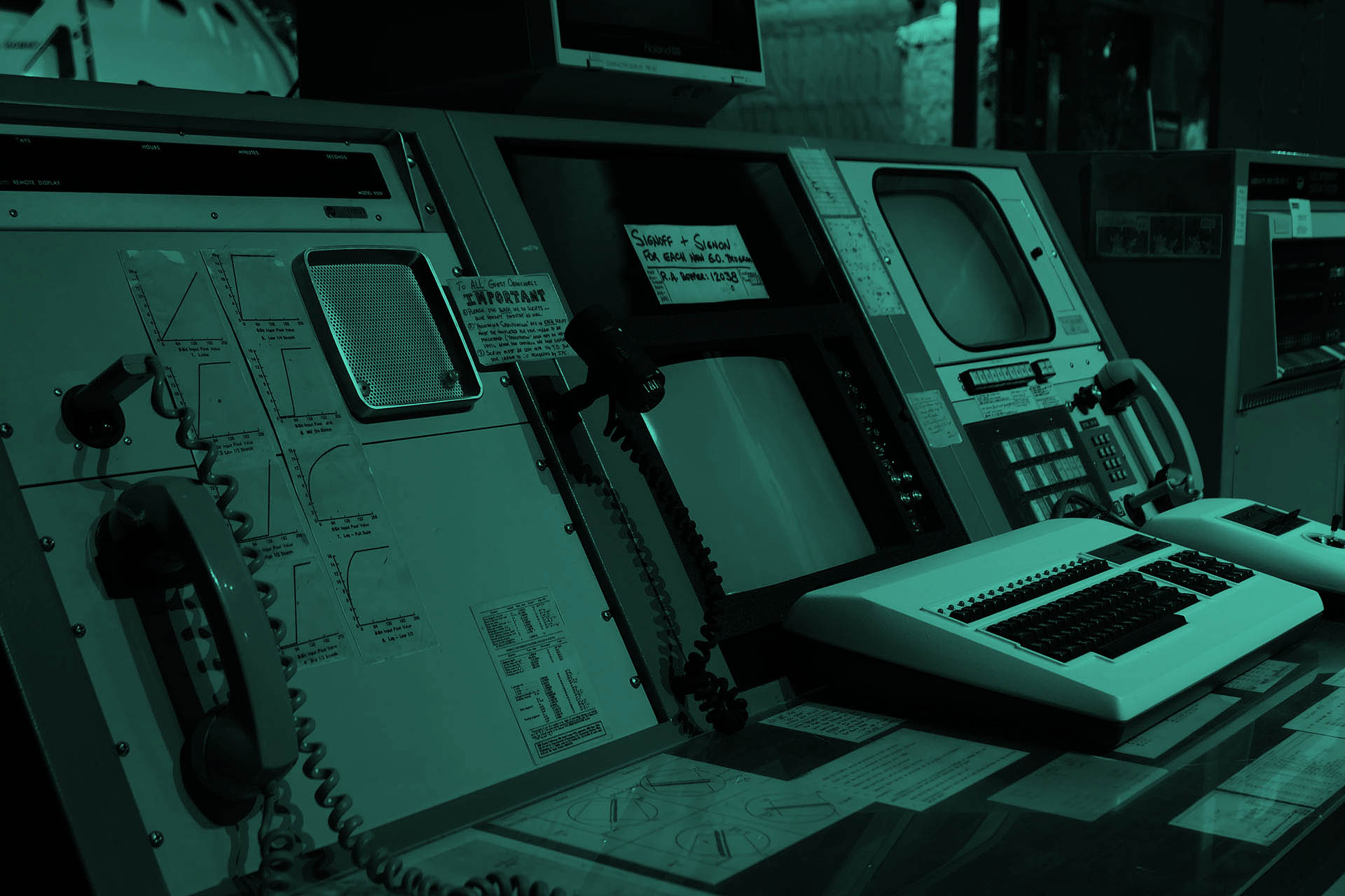Eine ziemlich alte Kommandozentrale mit verschiedenen Bildschirmen und einem Oldschool-Telefon.